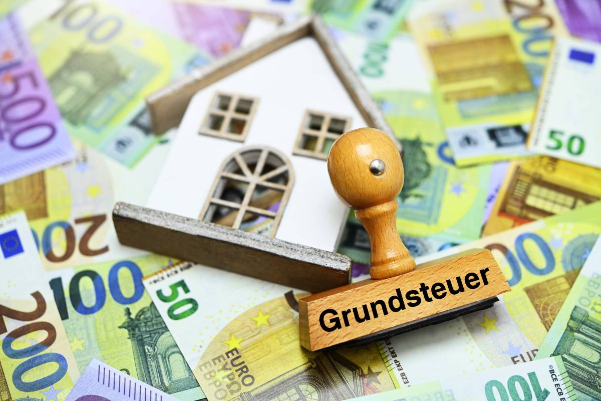 Haus und ein Stempel mit der Aufschrift "Grundsteuer" liegt auf Euro-Geldscheinen.