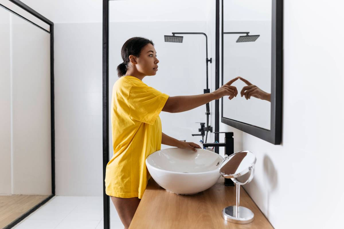 Frau steht im Bad und berührt ihr Spiegelbild