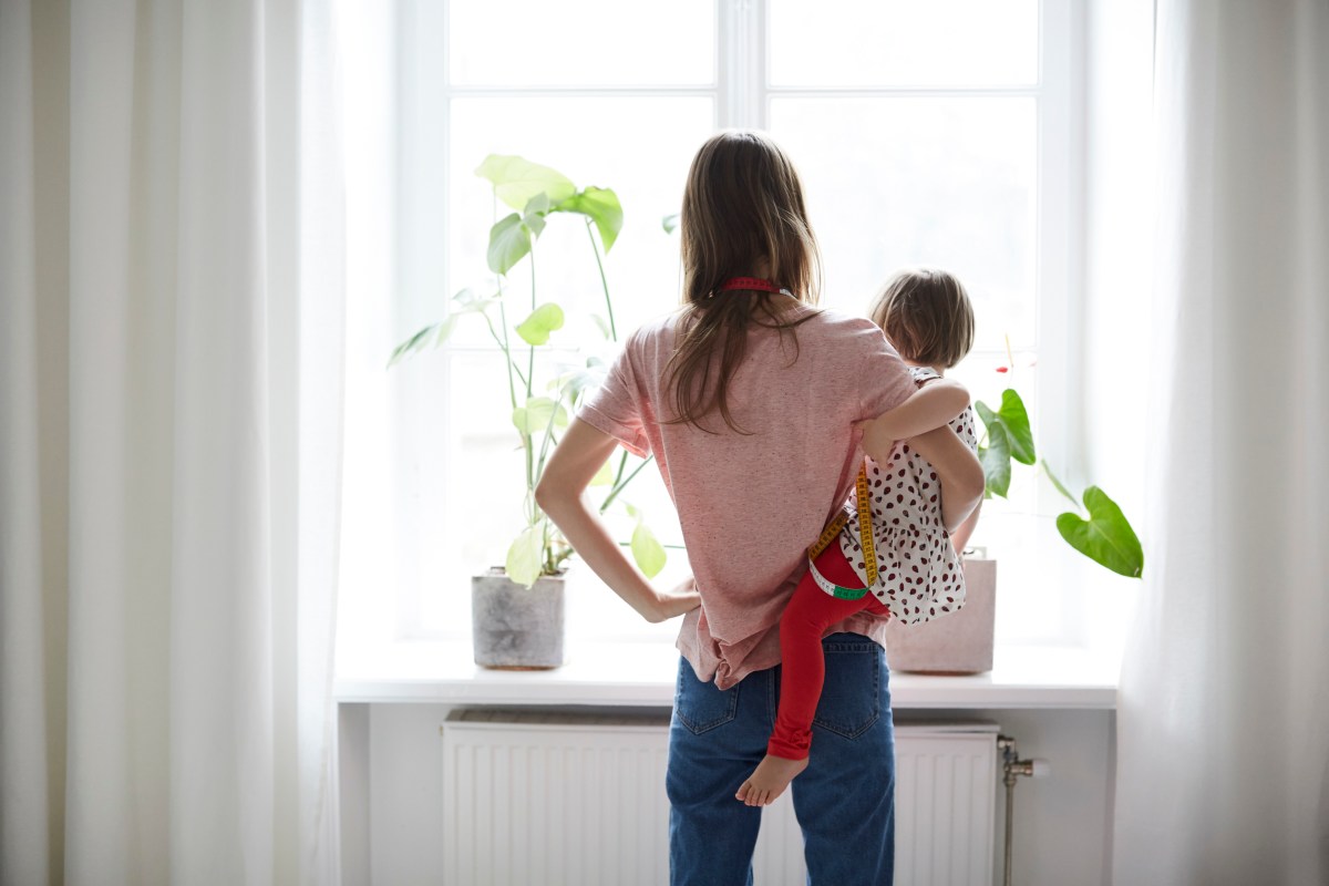 Frau hält Kind auf dem Arm und schaut aus dem Fenster