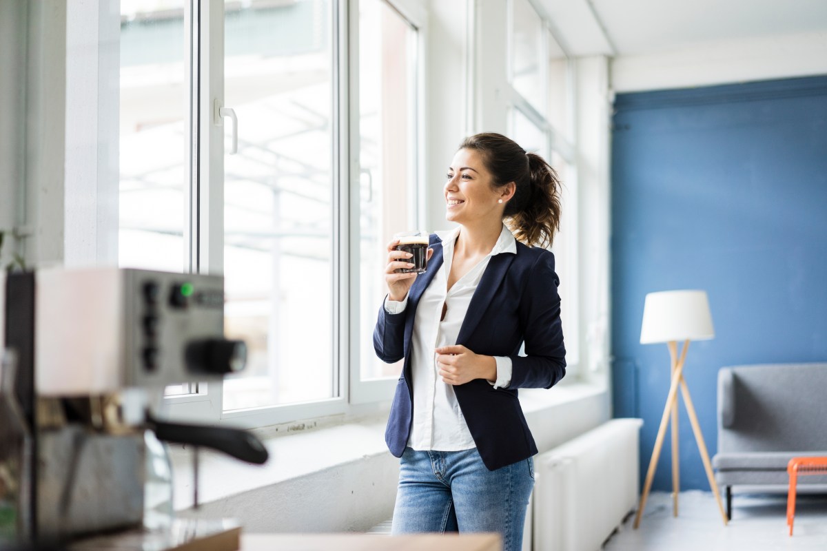 Frau trinkt im Büro eine Tasse Kaffee.