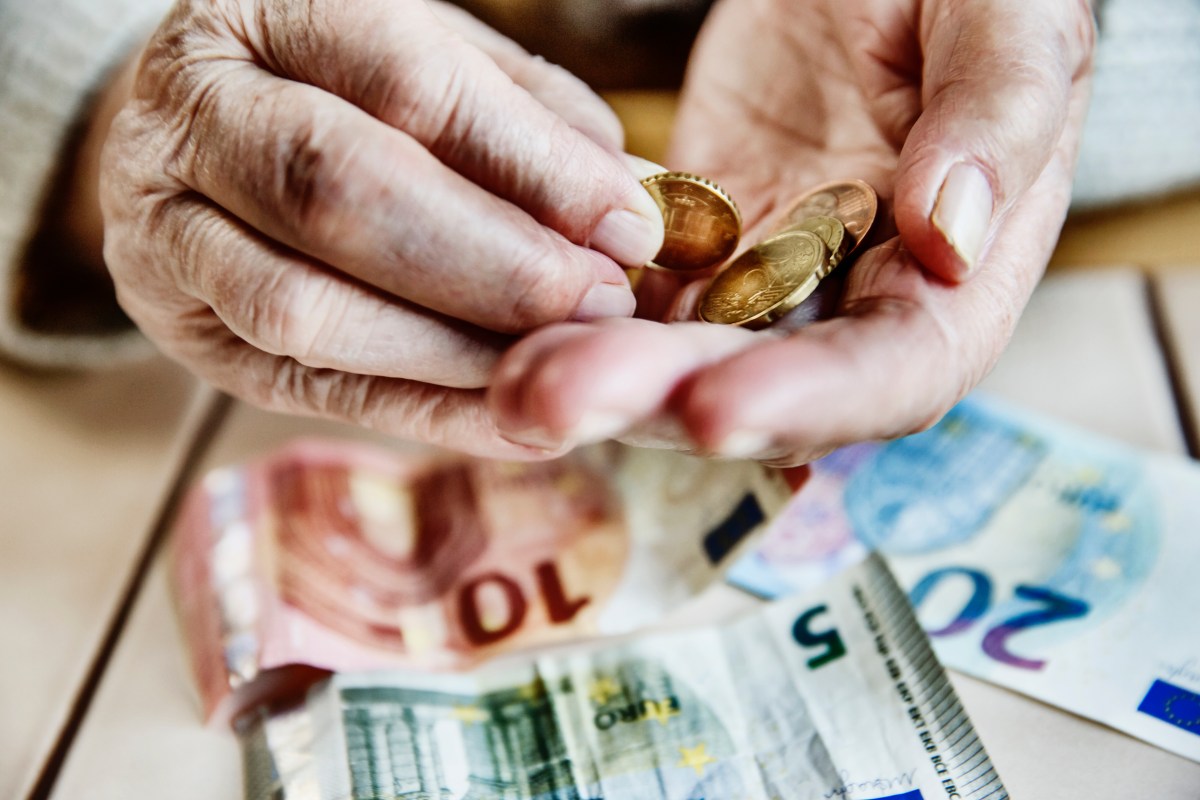 Eine ältere Person hält Münzen in der Hand. Darunter liegen Geldscheine.