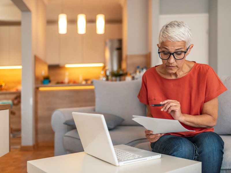 Eine ältere Frau sitzt vor dem laptop und füllt einen Antrag aus.