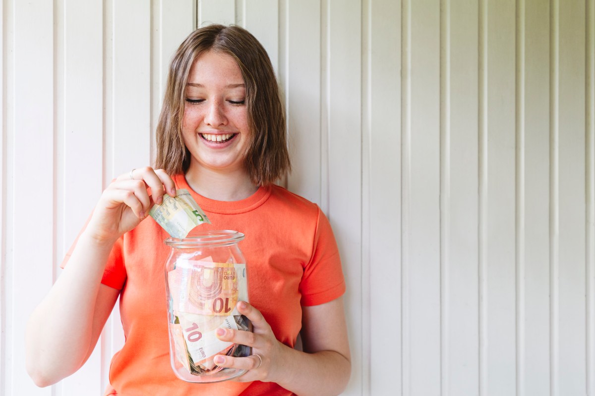 Junge Frau hält ein Glas mit Bargeld in der Hand.