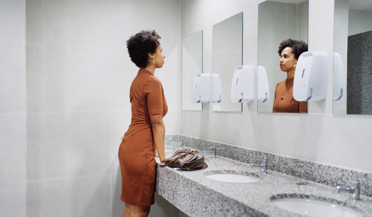 Frau schaut auf der Toilette in den Spiegel.