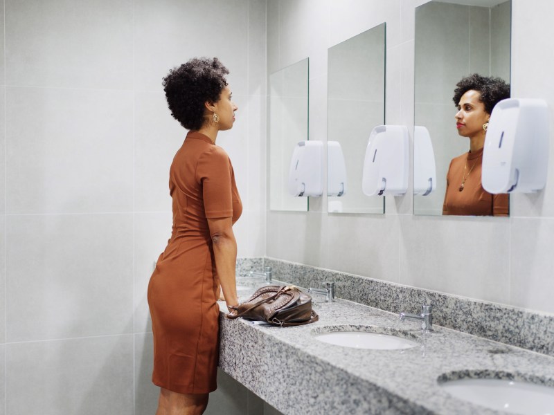 Frau schaut auf der Toilette in den Spiegel.