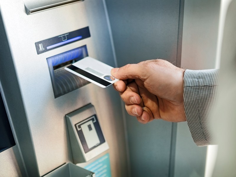 Hand steckt Bankkarte in einen Geldautomaten