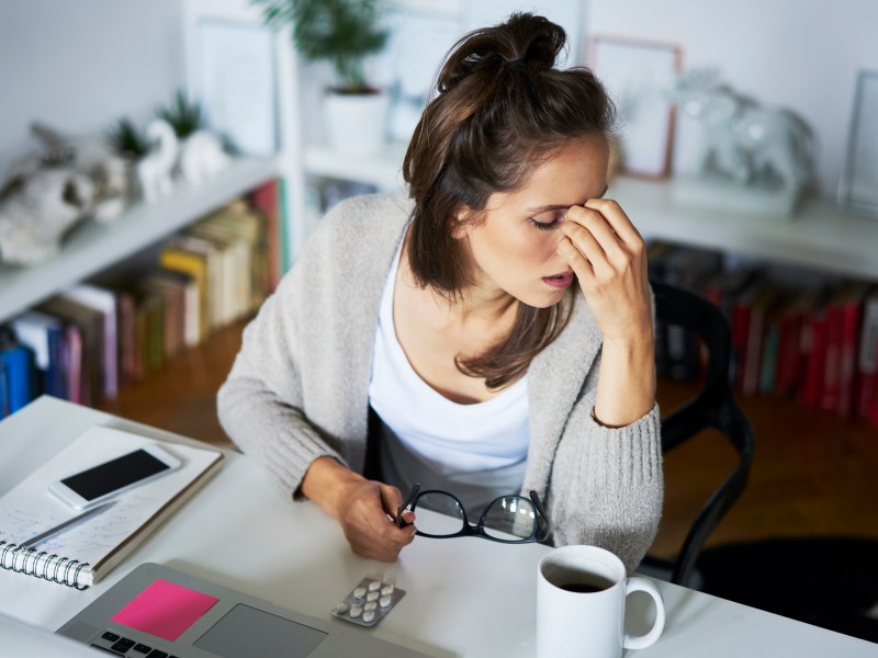 Junge Frau sitzt sehr erschöpft am Arbeitsplatz