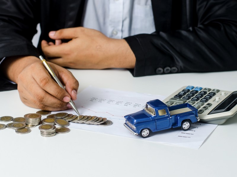 Ein Mann füllt seine Steuererklärung aus. Neben den Unterlagen liegen Münzen und ein Spielzeugauto.