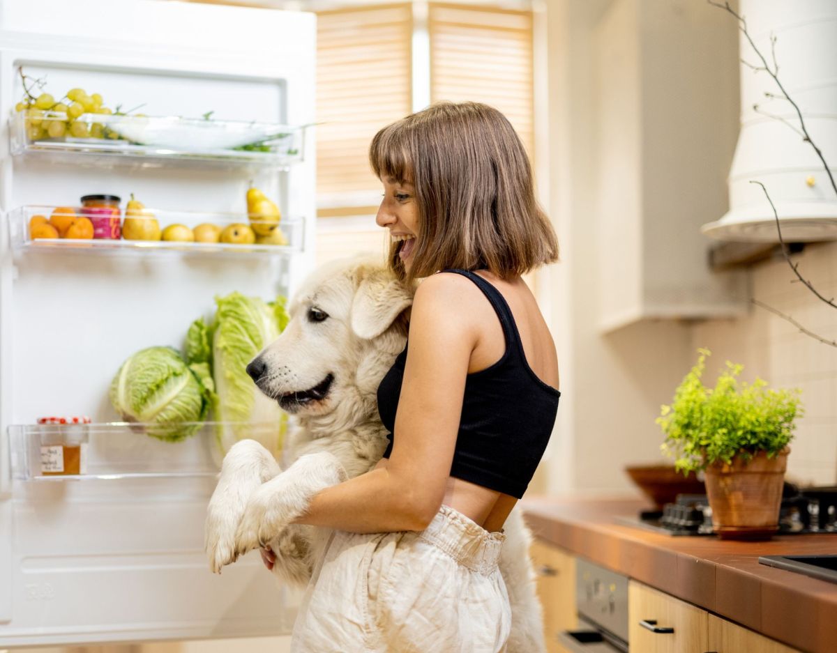 Frau mit Hund auf dem Arm steht vor Kühlschrank