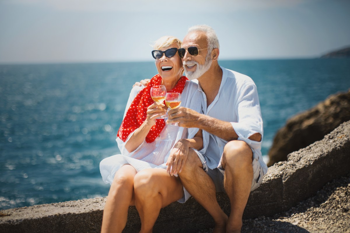 Ein Rentnerpärchen sitzt am Meer und trinkt Wein.