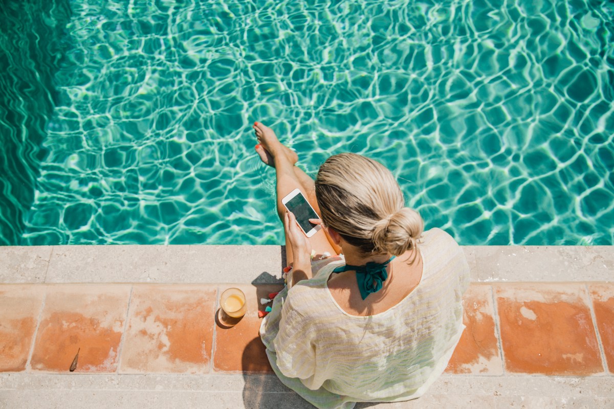 Eine Frau sitzt mit Handy am Pool.
