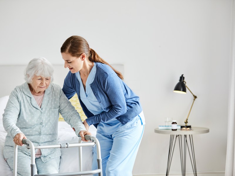 Pflegekraft hilft einer älteren Frau beim Aufstehen.