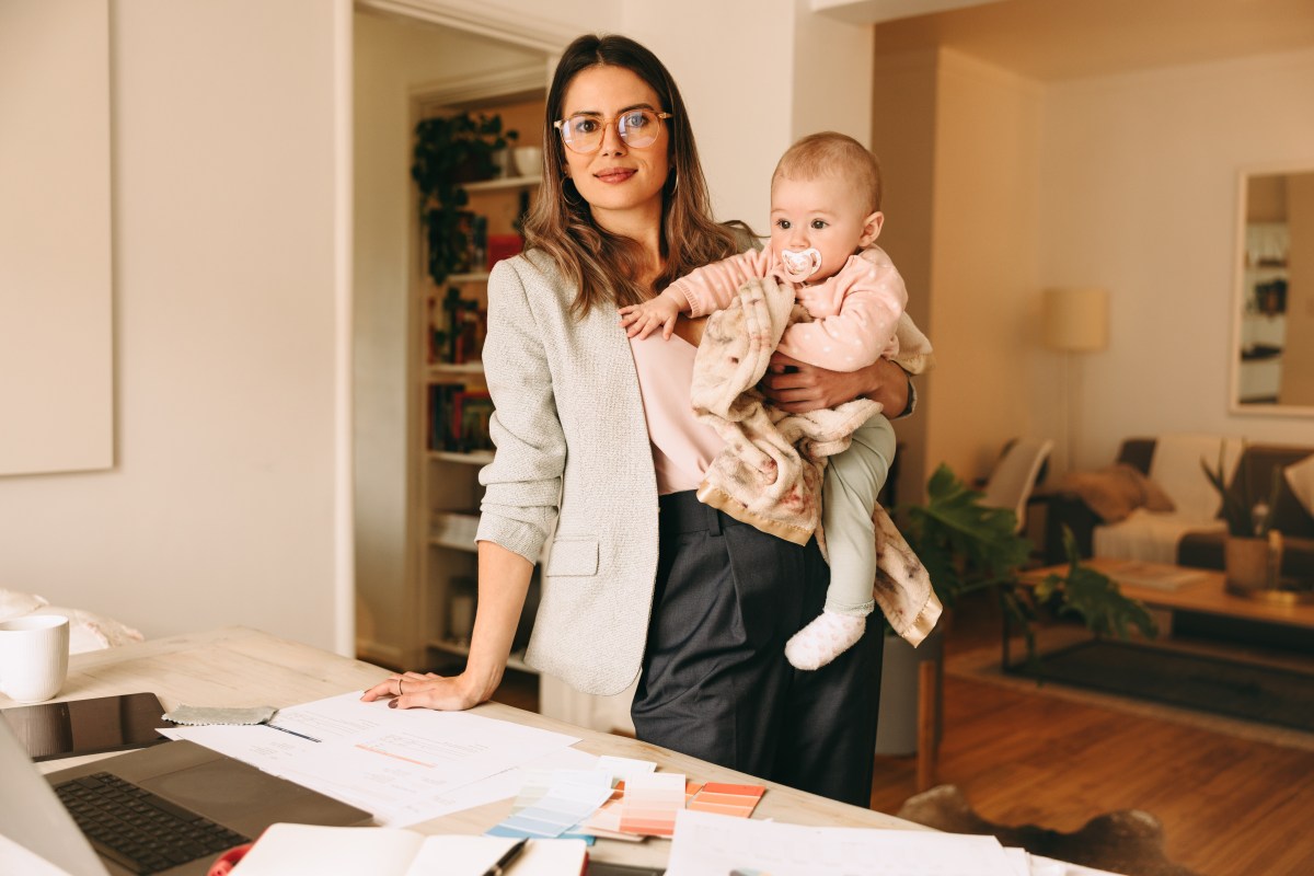 Eine Frau hält ein Baby auf dem Arm und steht vor einem Schreibtisch.