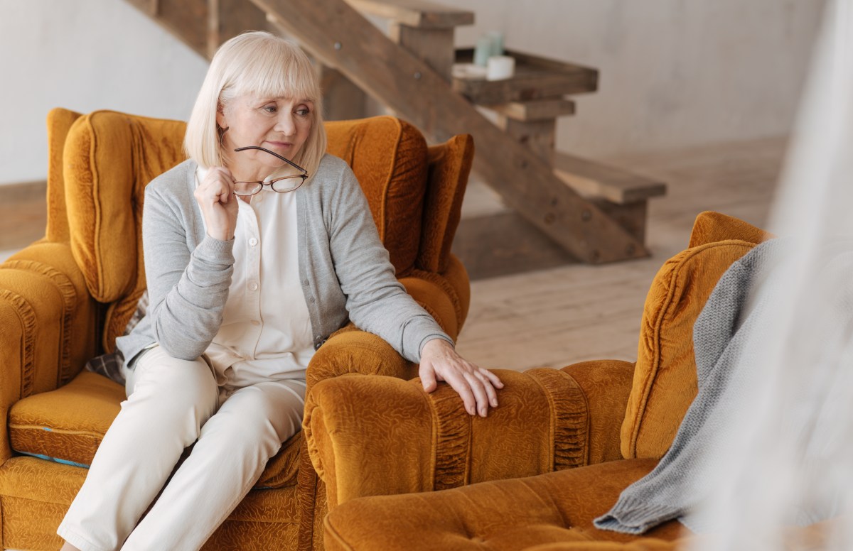 Eine Seniorin sitzt in ihrem Sessel und schaut auf einen leeren Platz.