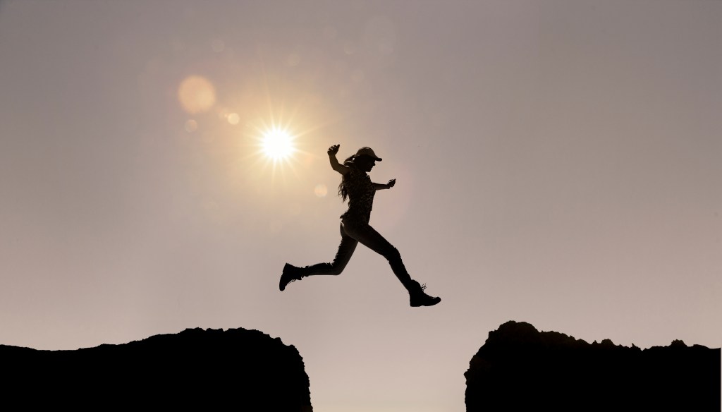 Eine Frau springt über eine Klippe. Die Sonne scheint.