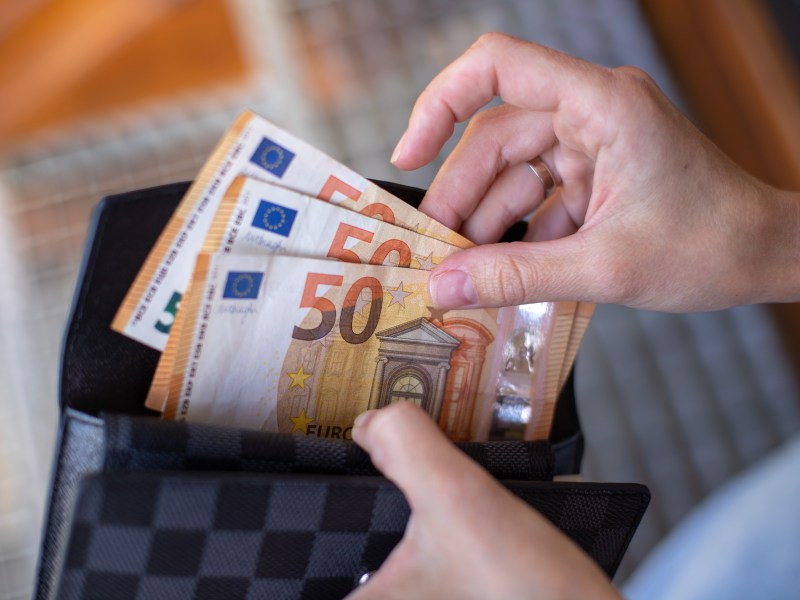 Eine Person zieht drei 50-Euro-Scheine aus einem Portemonnaie.