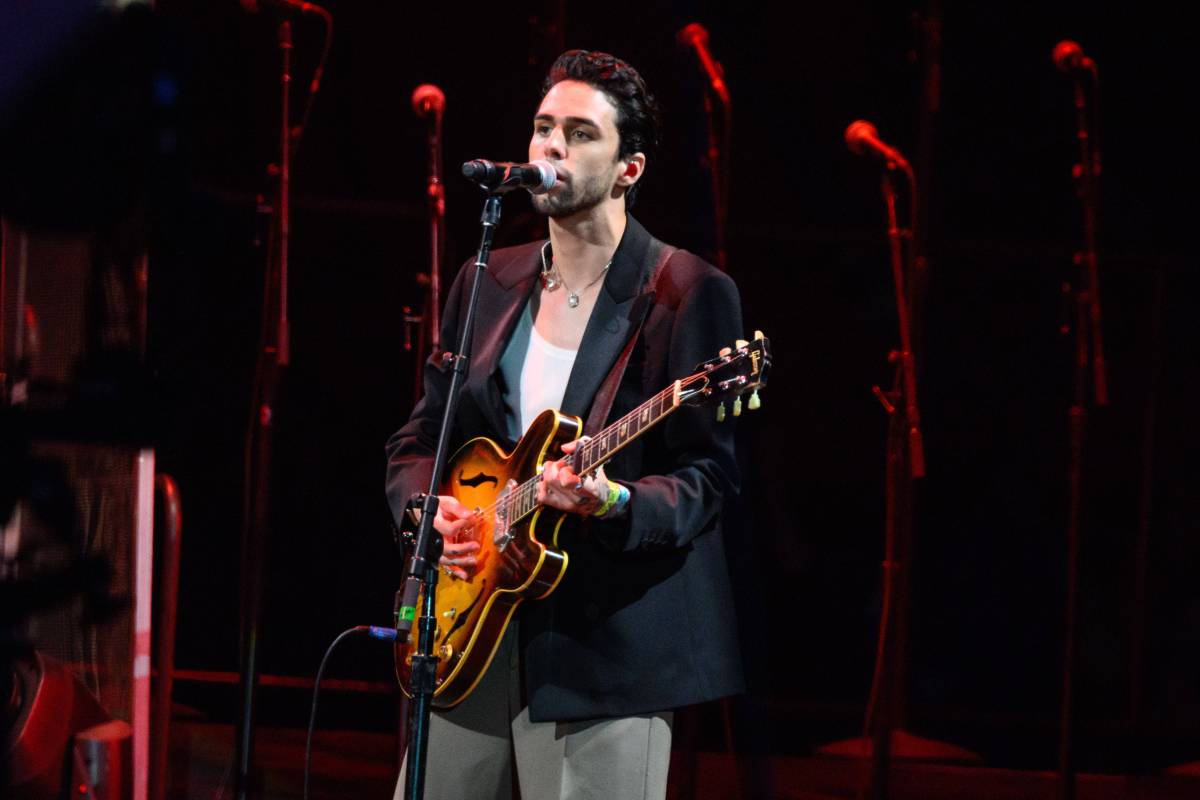 Sänger Stepehn Sanchez steht mit einer Gitarre auf einer Bühne und singt ins Mikrofon.