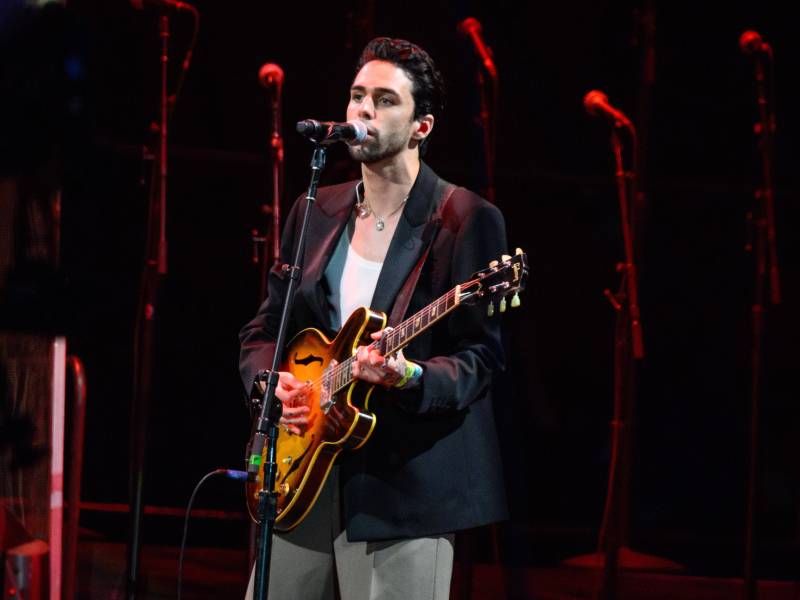 Sänger Stepehn Sanchez steht mit einer Gitarre auf einer Bühne und singt ins Mikrofon.