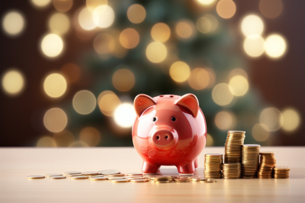 Eine Sparschwein samt Münzen steht vor einem Weihnachtsbaum.