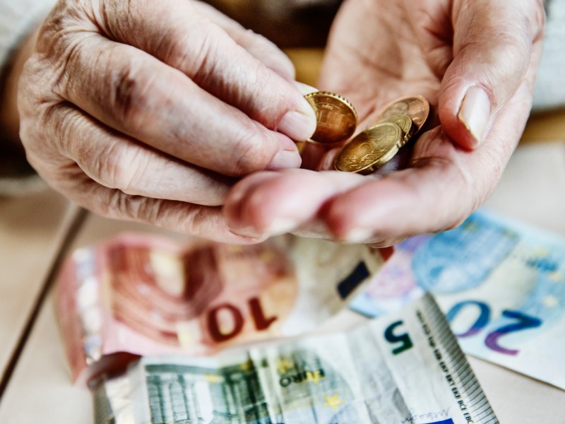 Eine ältere Person hält Münzen und Geldscheine in der Hand.