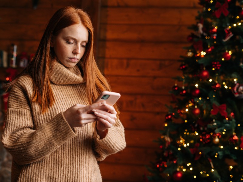 Eine Frau schaut konzentriert auf ihr Handy. Im Hintergrund steht ein Weihnachtsbaum.