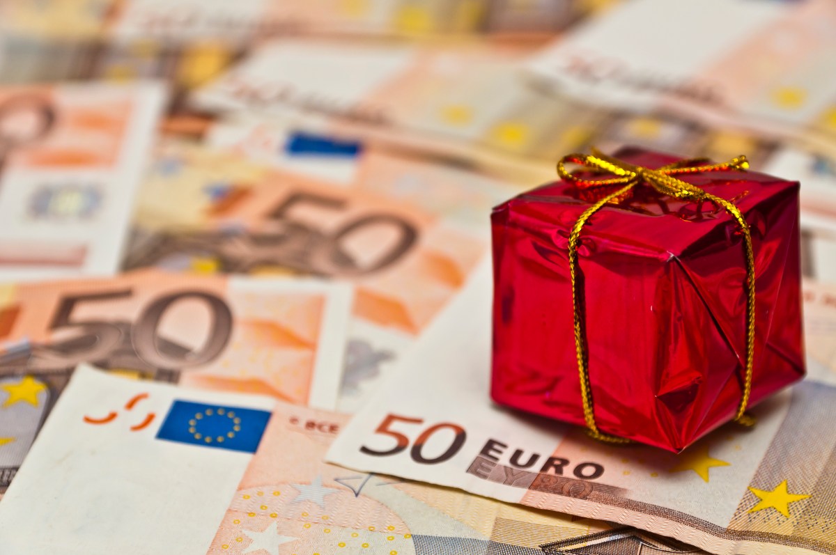 Ein kleines rotes Geschenk steht auf 50-Euro-Scheinen.