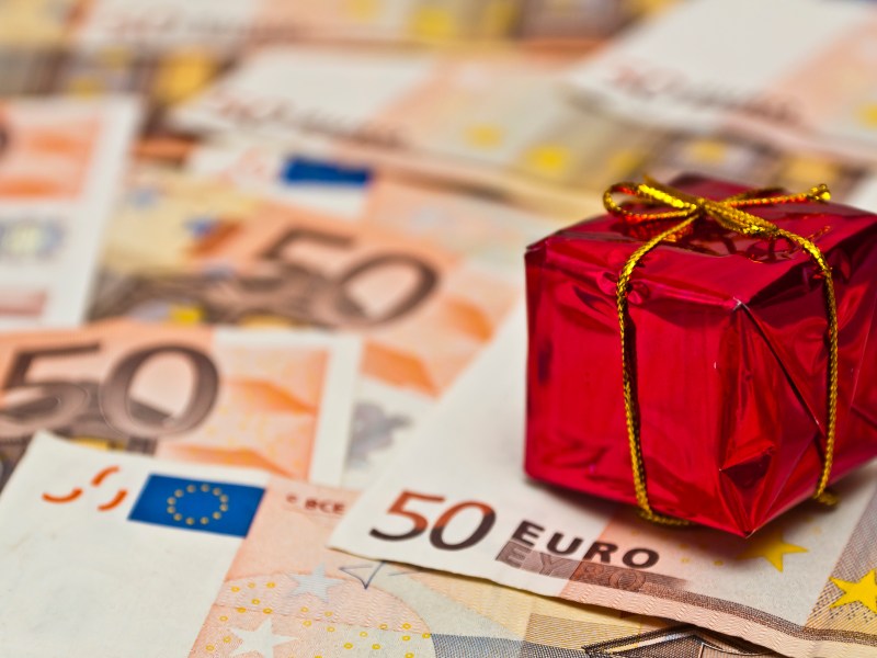 Ein kleines rotes Geschenk steht auf 50-Euro-Scheinen.
