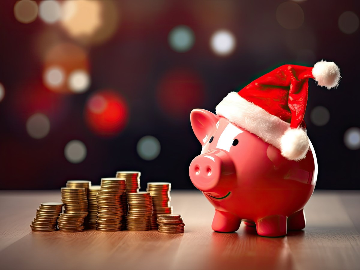 Neben einem Sparschwein mit Weihnachtsmütze stehen Münzen.