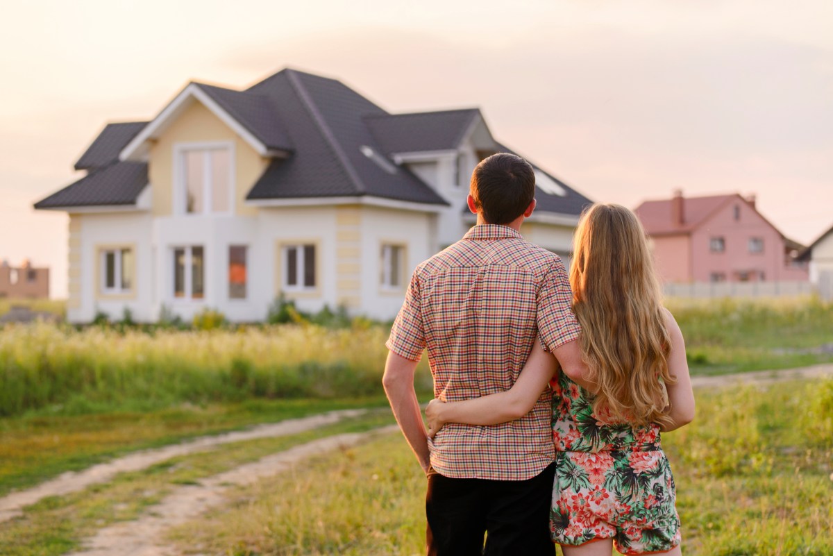 Eine Frau und ein Mann stehen Arm in Arm vor einem Haus.