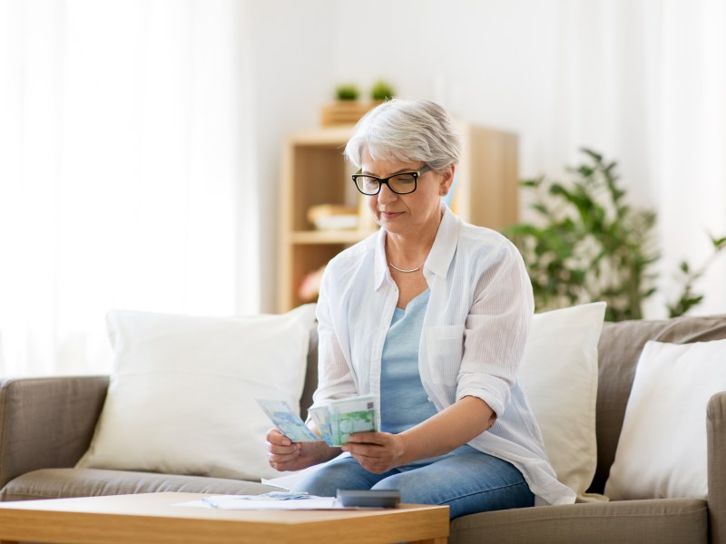 Eine Seniorin sitzt auf der Couch und hält Geld in der Hand.