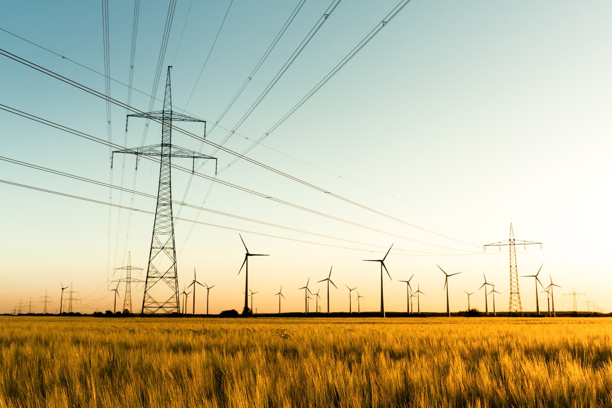 Strommasten im Kornfeld und Windräder im Sonnenuntergang.