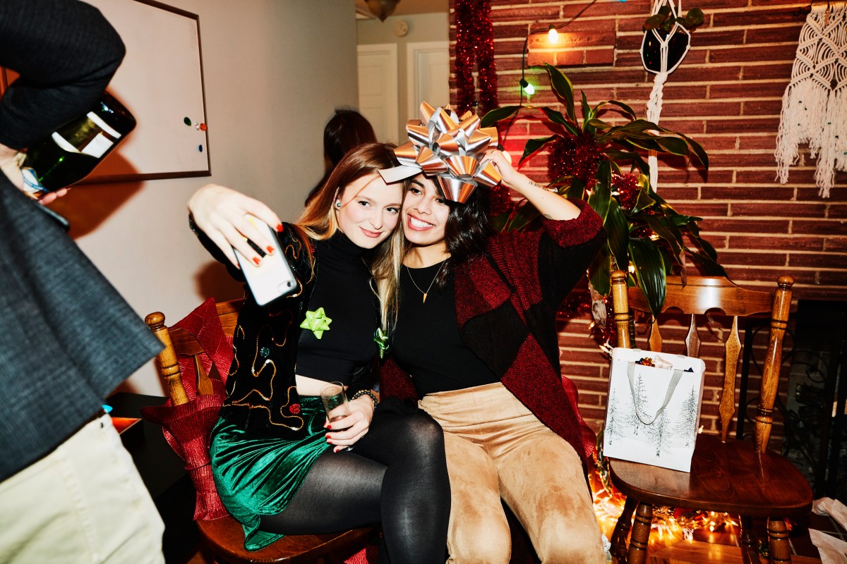 Lächelnde Freundinnen posieren für ein Selfie mit einer Schleife über dem Kopf während der Weihnachtsfeier.