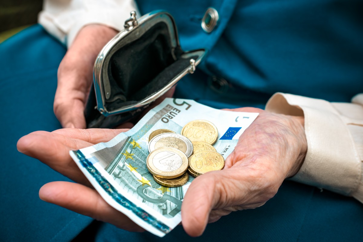 In einer Hand eines Seniors oder einer Seniorin liegt ein Fünf-Euro-Schein und Münzen.