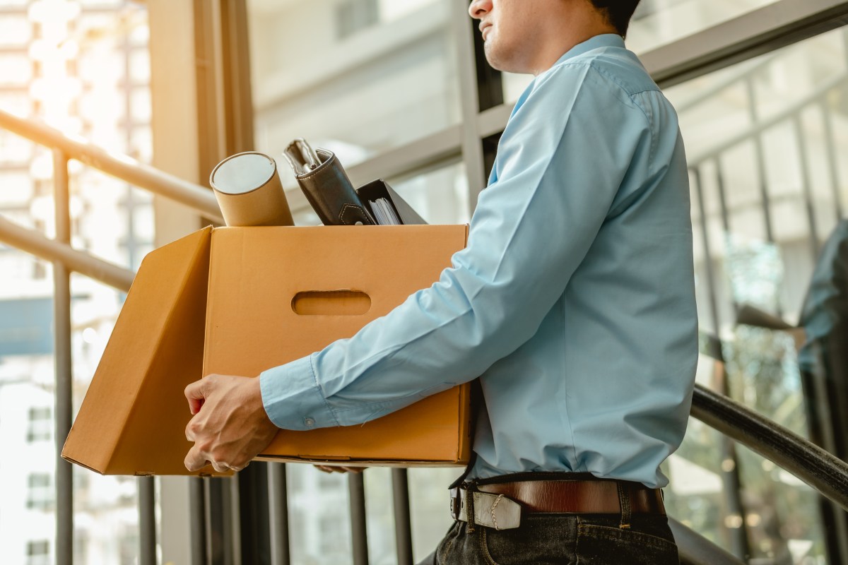 Ein Mann trägt einen Karton mit Gegenständen aus dem Büro.