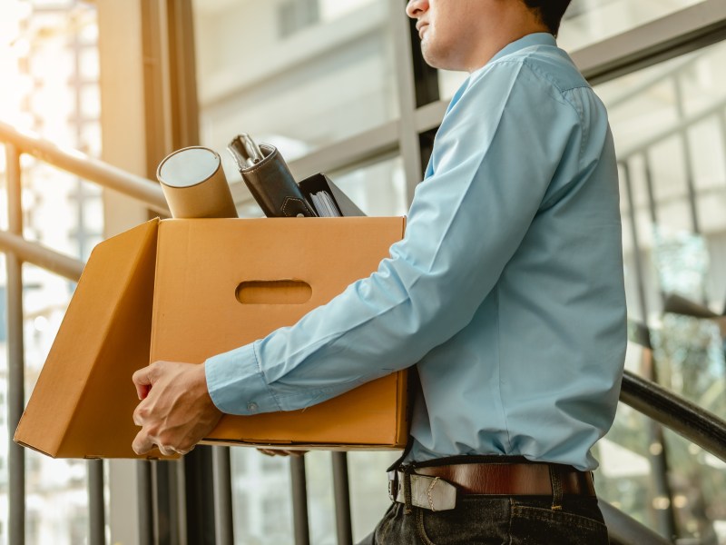 Ein Mann trägt einen Karton mit Gegenständen aus dem Büro.