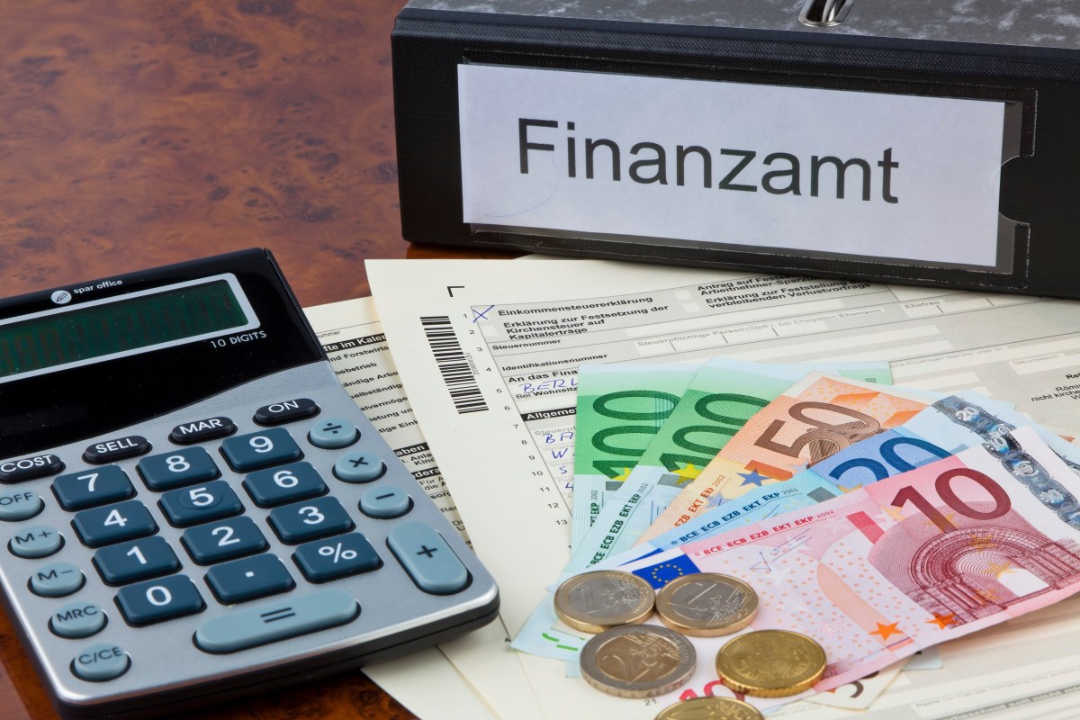 Ein Taschenrechner, Geld und Steuerunterlagen liegen neben einem Ordner mit der Aufschrift "Finanzamt".