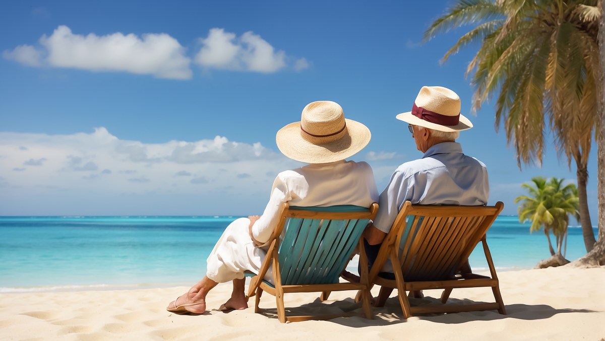 Ein Senioren-Paar sitzt am Strand unter Palmen.