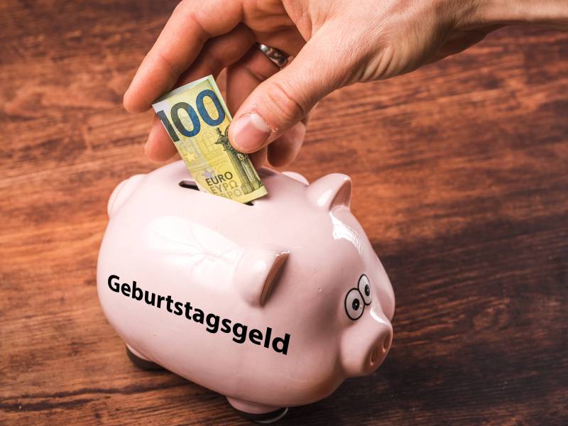 In ein Sparschwein mit der Aufschrift "Geburtstagsgeld" wird ein 100-Euro-Schein reingesteckt.