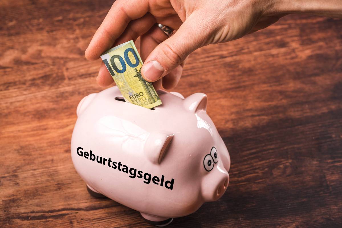 In ein Sparschwein mit der Aufschrift "Geburtstagsgeld" wird ein 100-Euro-Schein reingesteckt.