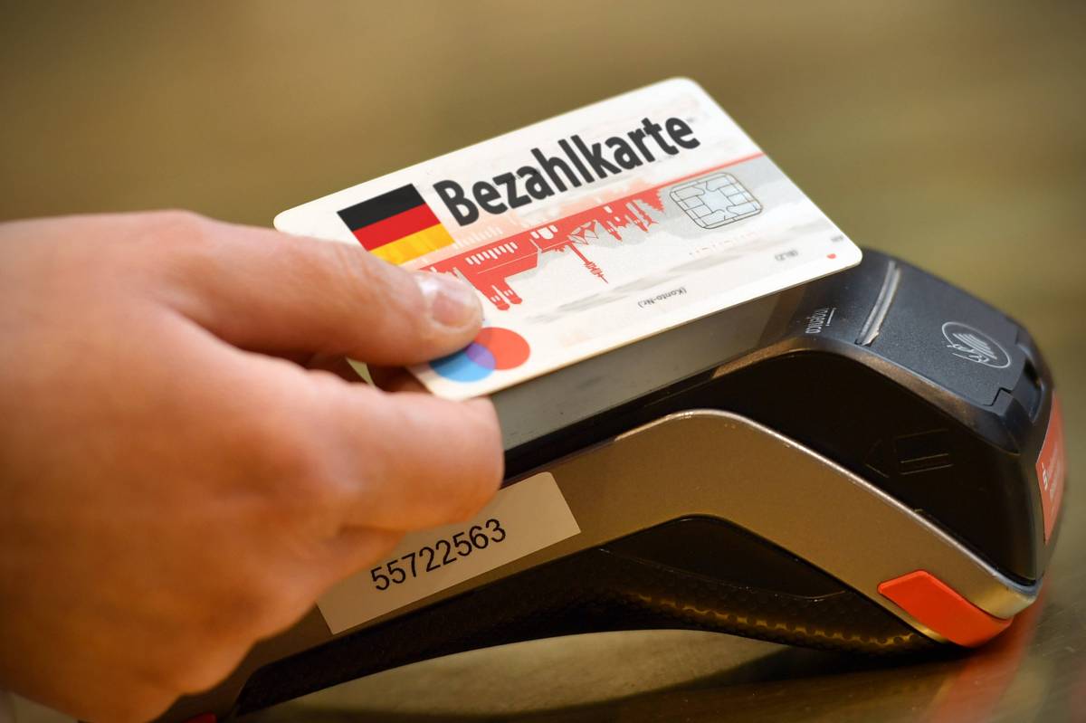 Eine Person hält eine Bezahlkarte an Kartenlesegerät.