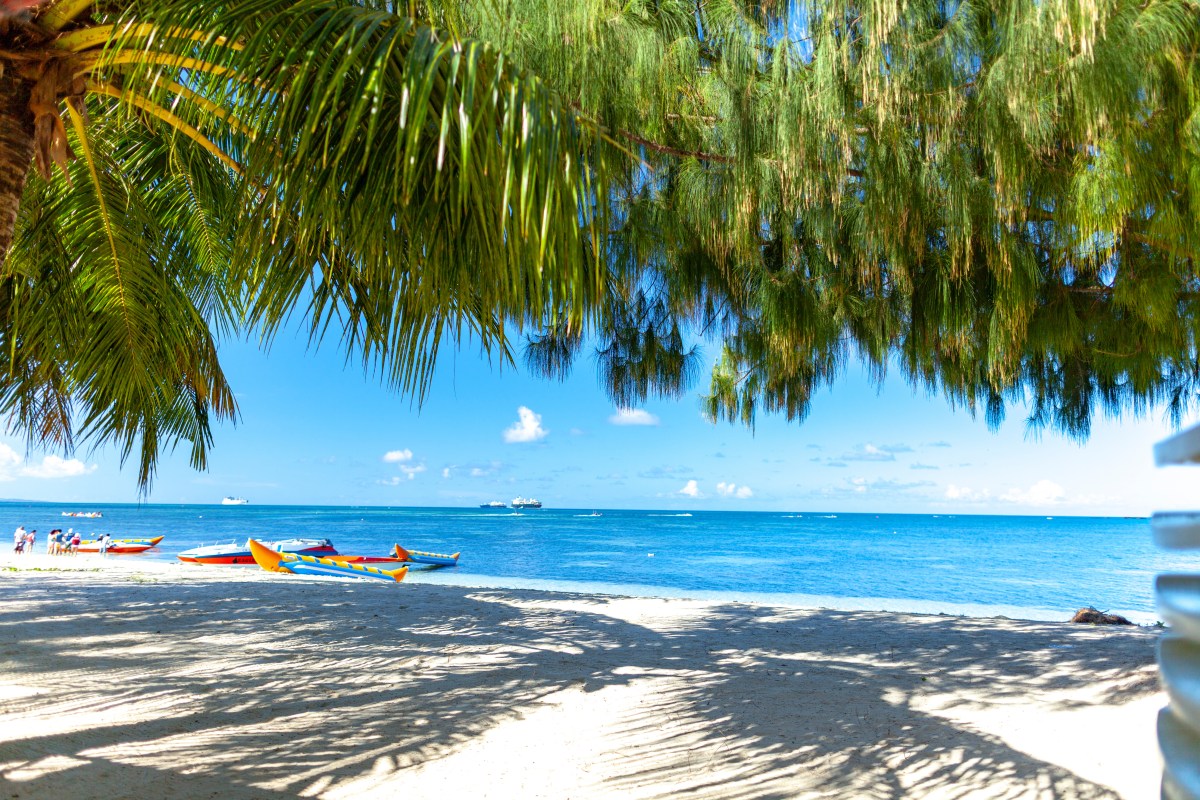 Ein weißer Sandstrand mit Palmen und blauem Wasser.