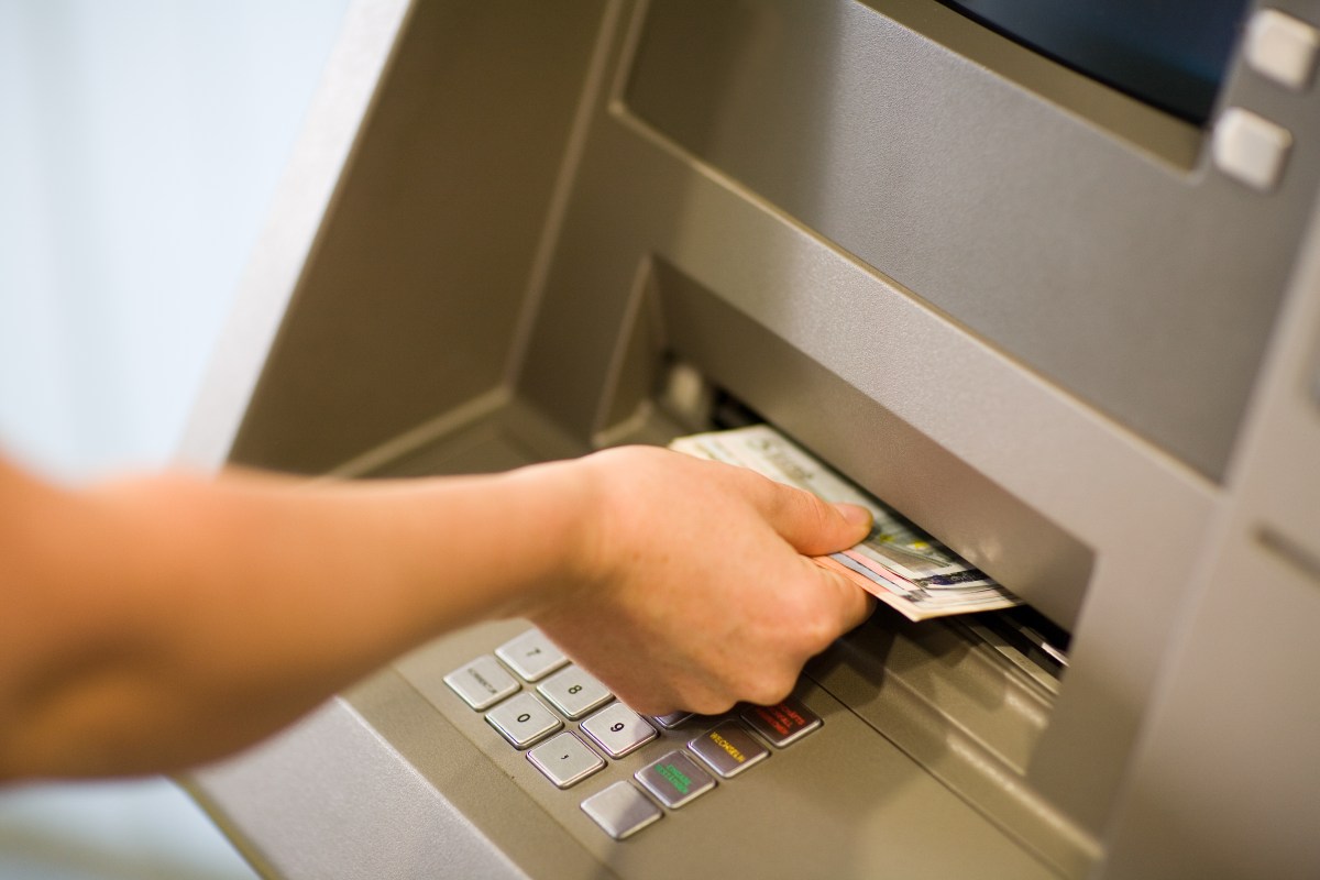 Eine Person nimmt Geldscheine aus dem Fach eines Bankautomaten.