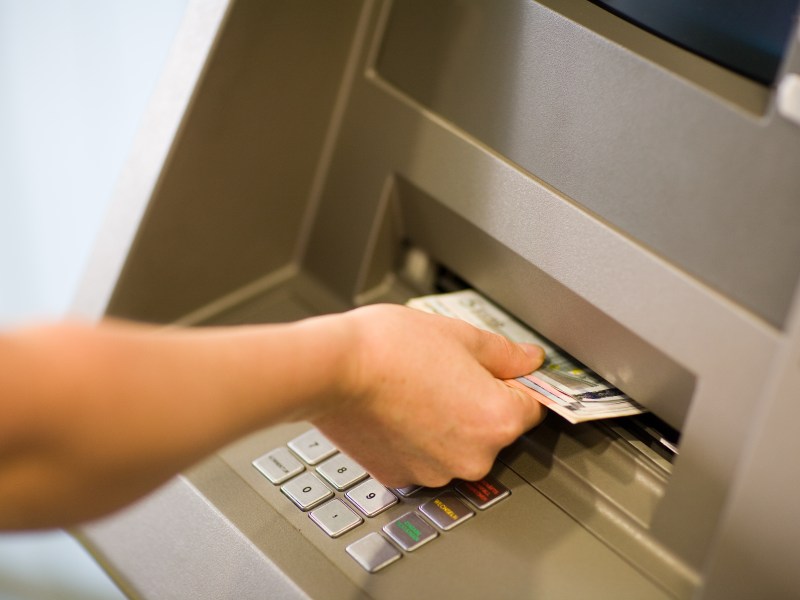 Eine Person nimmt Geldscheine aus dem Fach eines Bankautomaten.