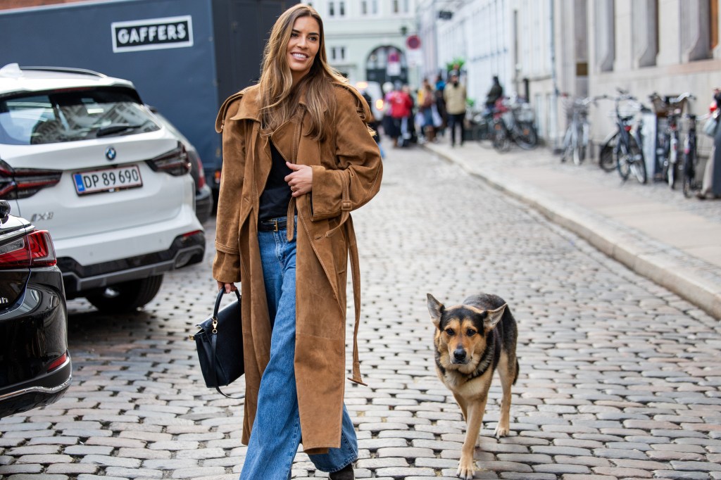 Eine Frau mit Schäferhund trägt einen Trenchcoat.