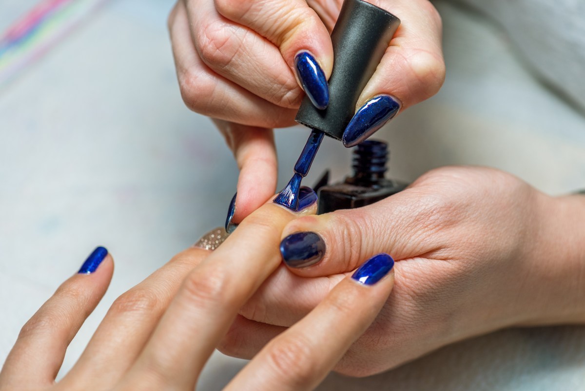 Frau kriegt die Nägel in einem dunklen Blau lackiert.