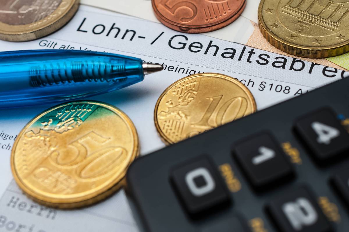 Auf einer Gehaltsabrechnung liegen Münzen, ein Kugelschreiber und ein Taschenrechner.