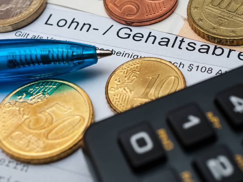 Auf einer Gehaltsabrechnung liegen Münzen, ein Kugelschreiber und ein Taschenrechner.