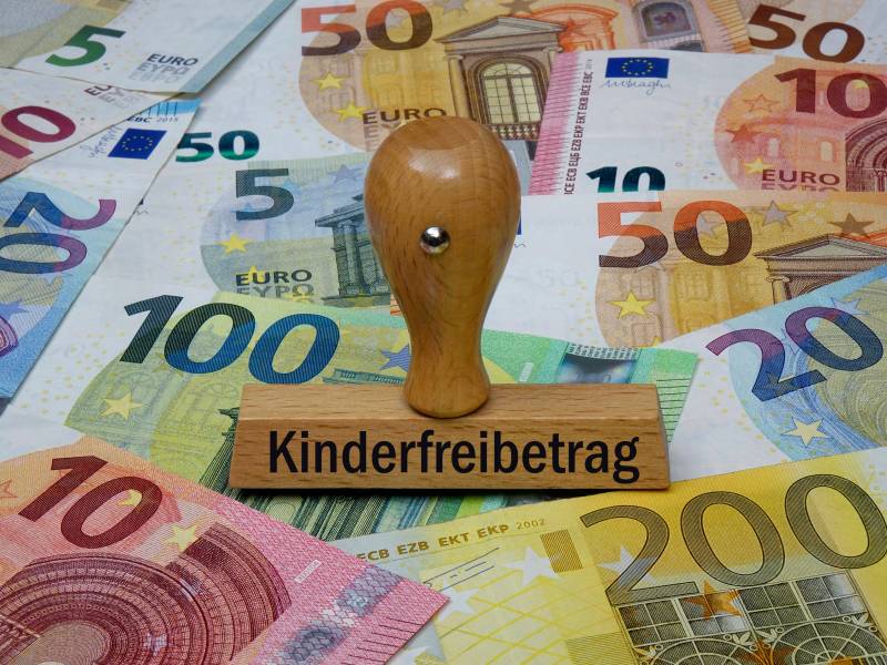 Auf einem Holzstempel steht das Wort "Kindergeld". Darunter liegen Geldscheine.