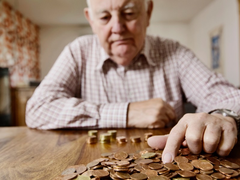 Ein Senior sitzt am Tisch und zählt Münzen.