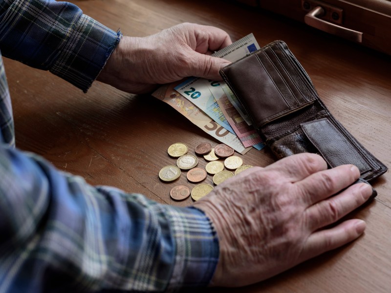 Ein Senior hat sein Portemonnaie geöffnet. Davor liegen Münzen und Geldscheine.
